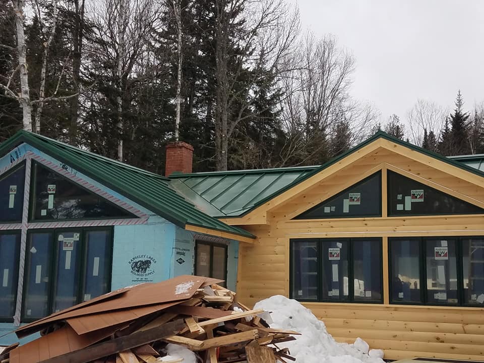 Vibrant green seam metal roofing on pine log cabin with large front windows